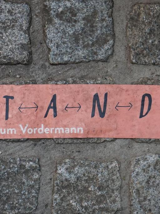 Aufkleber mit den Worten „S T A N D halten“ auf Kopfsteinpflaster in Erfurt.