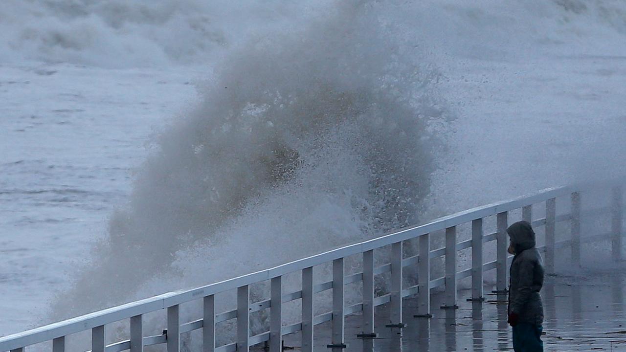 Eine Frau beobachtet eine über die Strandpromenade schlagende Welle. Eine Frau beobachtet eine über die Strandpromenade schlagende Welle.