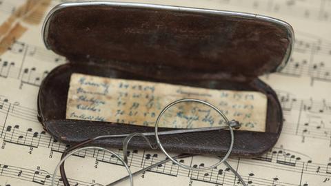 Eine Brille liegt mit einem Etui und handschriftlichen Notizen auf einem Notenblatt.