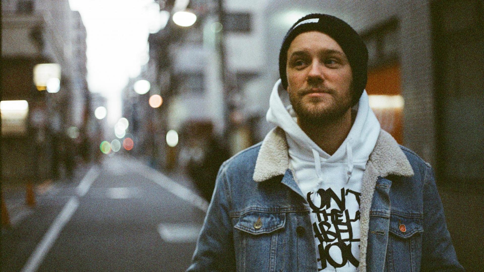 Der Hip Hopper Juse Ju mit Mütze in einer Jeans Jacke und mit weißem Hoodie darunter steht in einer leeren Strassenflucht Der Hip Hopper Juse Ju mit Mütze in einer Jeans Jacke und mit weißem Hoodie darunter steht in einer leeren Strassenflucht