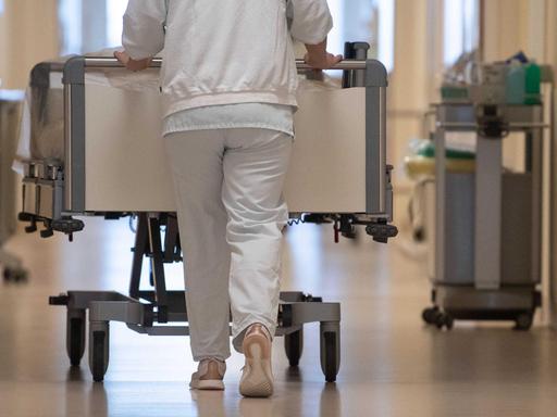 Eine Krankenpflegerin schiebt ein Krankenbett durch einen Flur.