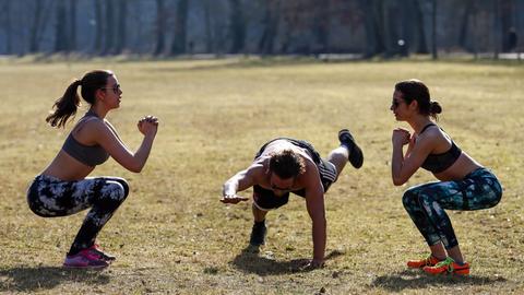 Zwei junge Frauen und ihr Trainer machen am 22.02.2015 im Stadtpark Hain in Bamberg ein Workout in der Sonne.