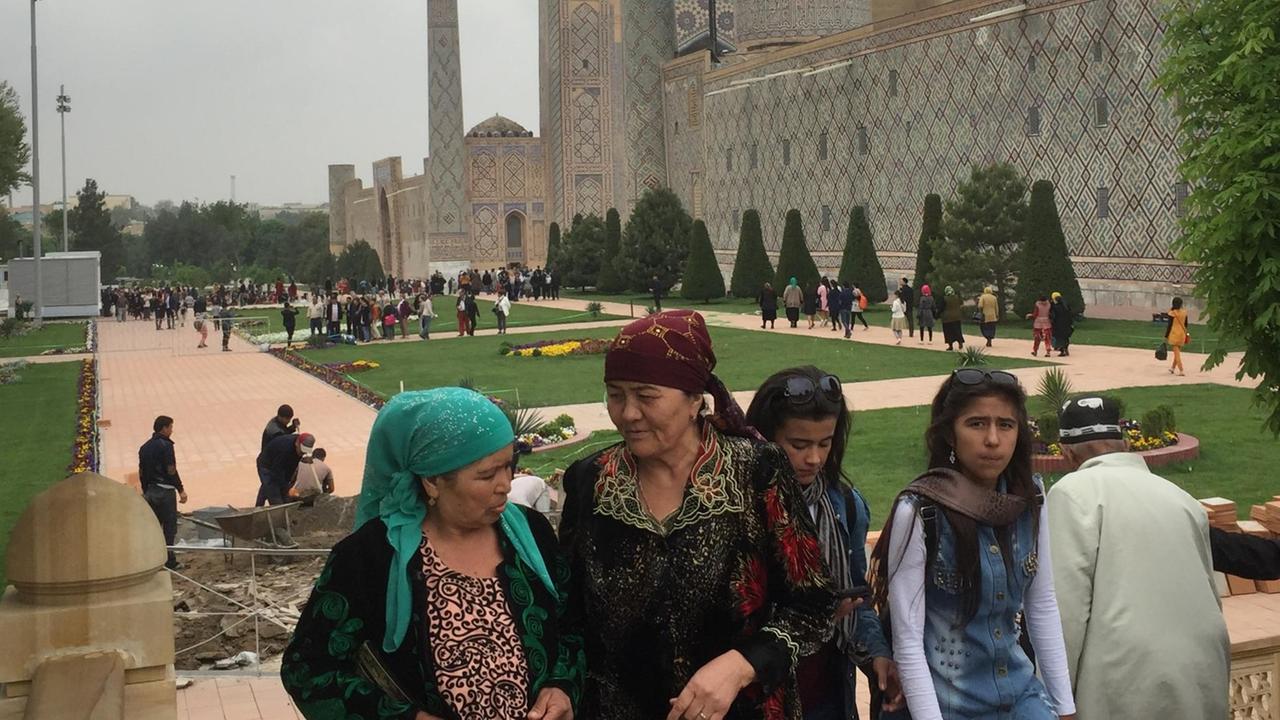 Junge und alte Frauen stehen nebeneinander, im Hintergrund ist eine Moschee zu sehen.