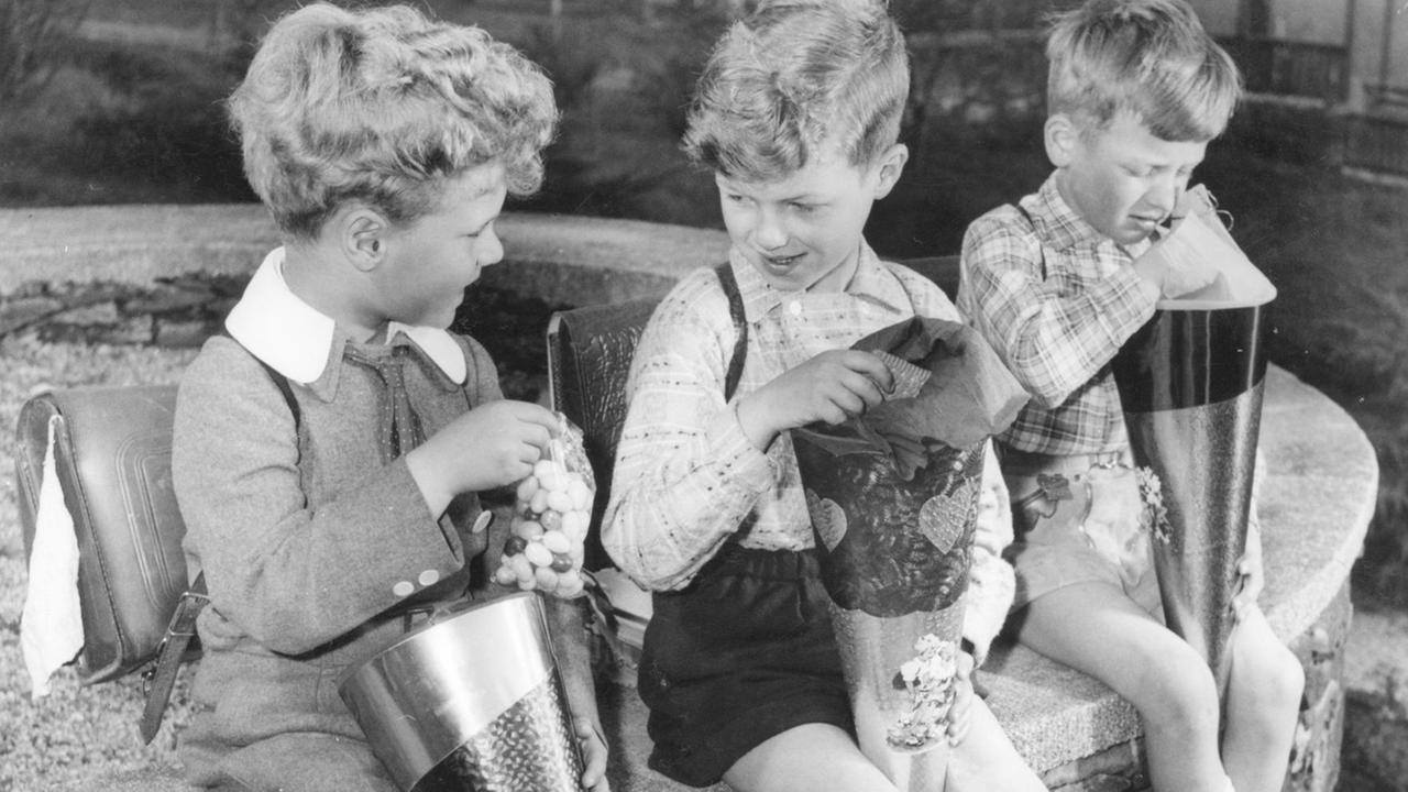 Am Tag der Einschulung ditzen drei Jungen mit Schultüten und ihren Süßigkeiten auf einer Mauer. Am Tag der Einschulung ditzen drei Jungen mit Schultüten und ihren Süßigkeiten auf einer Mauer.