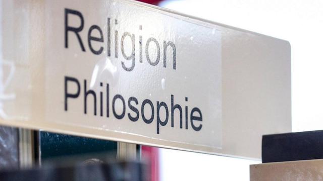 In einer Bibliothek sind auf einem Schild über einem Bücherregal die Worte Religion und Philosophie zu lesen.