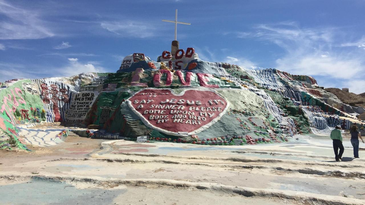 Ein bunter Hügel in Slab City mit Sprüchen und einem Kreuz ganz oben. Ein bunter Hügel in Slab City mit Sprüchen und einem Kreuz ganz oben.