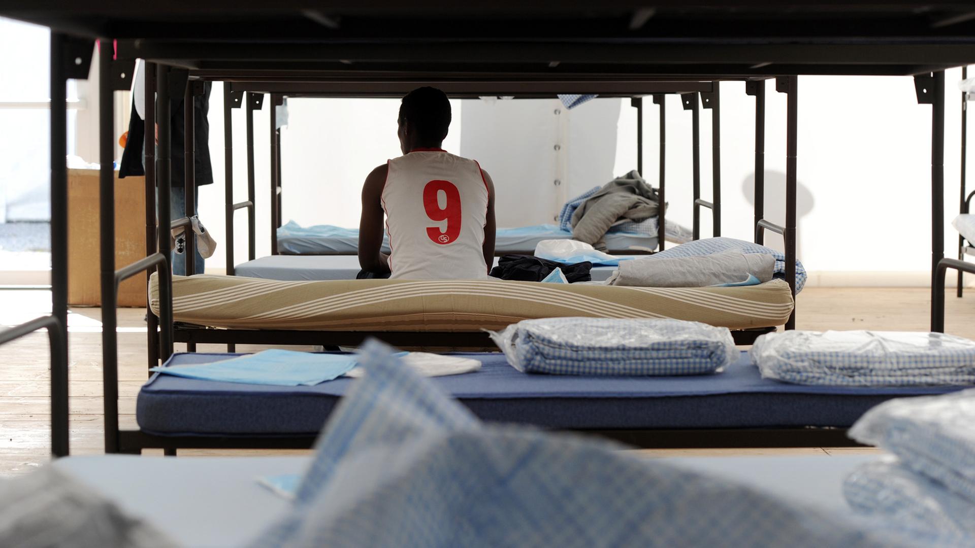 Ein Flüchtling sitzt in München in einem Unterkunftszelt am Internationalen Jugendübernachtungscamp am Kapuzinerhölzl in seinem Bett.