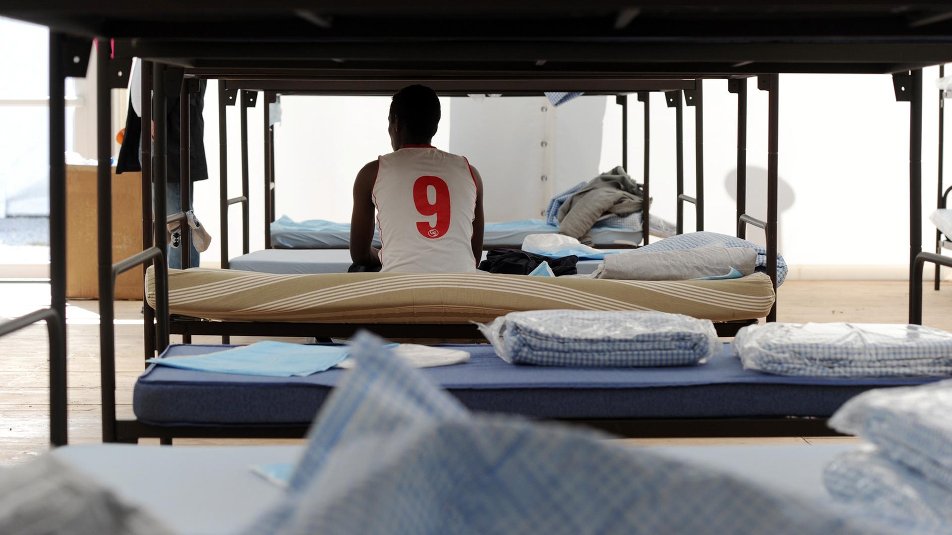 Ein Flüchtling sitzt in München in einem Unterkunftszelt am Internationalen Jugendübernachtungscamp am Kapuzinerhölzl in seinem Bett. Ein Flüchtling sitzt in München in einem Unterkunftszelt am Internationalen Jugendübernachtungscamp am Kapuzinerhölzl in seinem Bett.