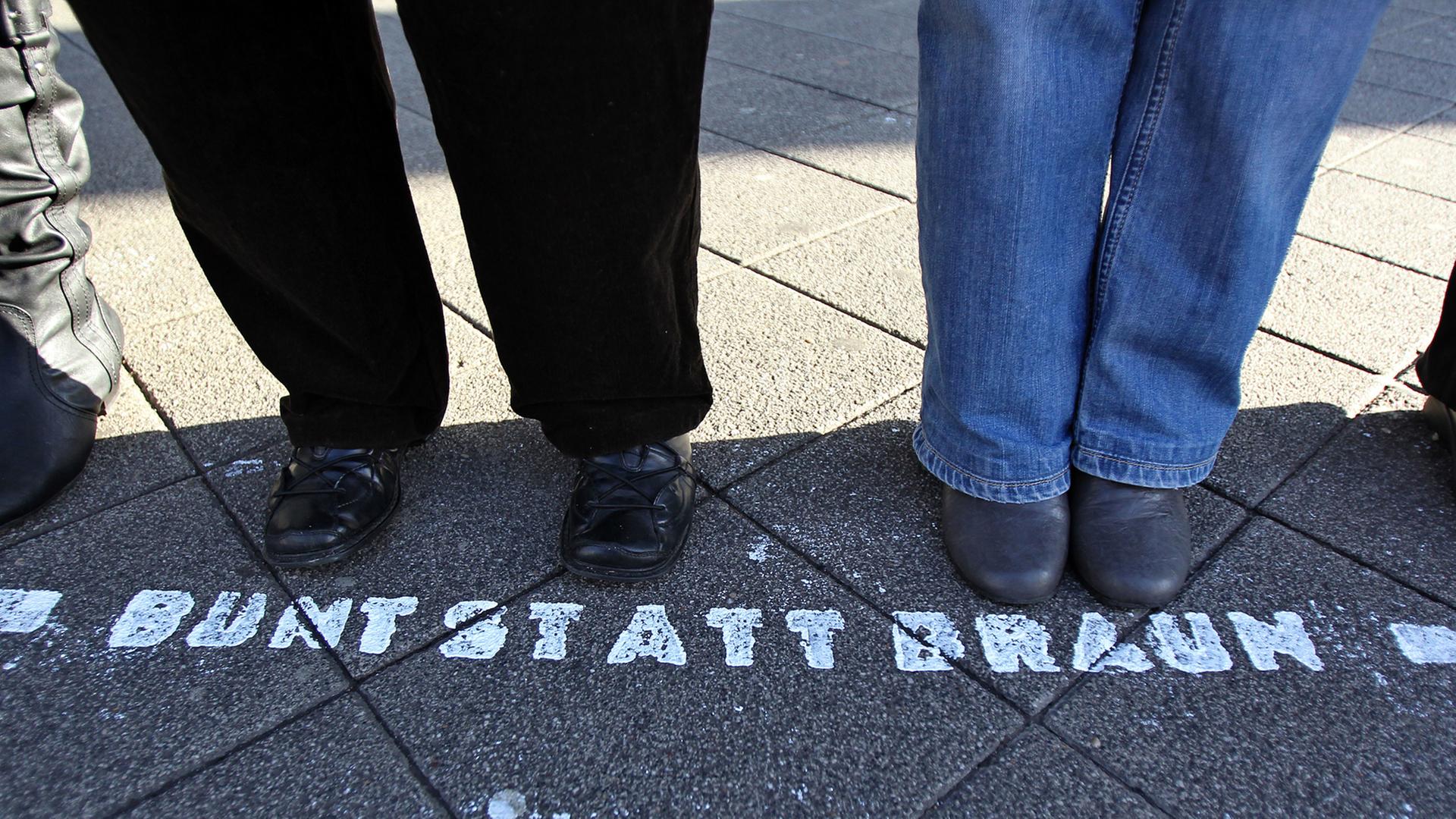 Füße einer Menschenkette bei einem Protest gegen Neonzais. Vor den Füßen steht auf der Straße "Bunt statt Braun" Füße einer Menschenkette bei einem Protest gegen Neonzais. Vor den Füßen steht auf der Straße "Bunt statt Braun"