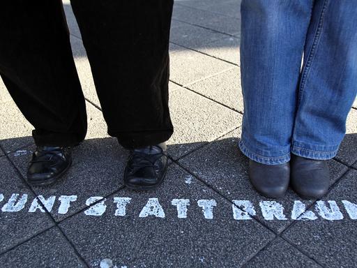 Füße einer Menschenkette bei einem Protest gegen Neonzais. Vor den Füßen steht auf der Straße "Bunt statt Braun"