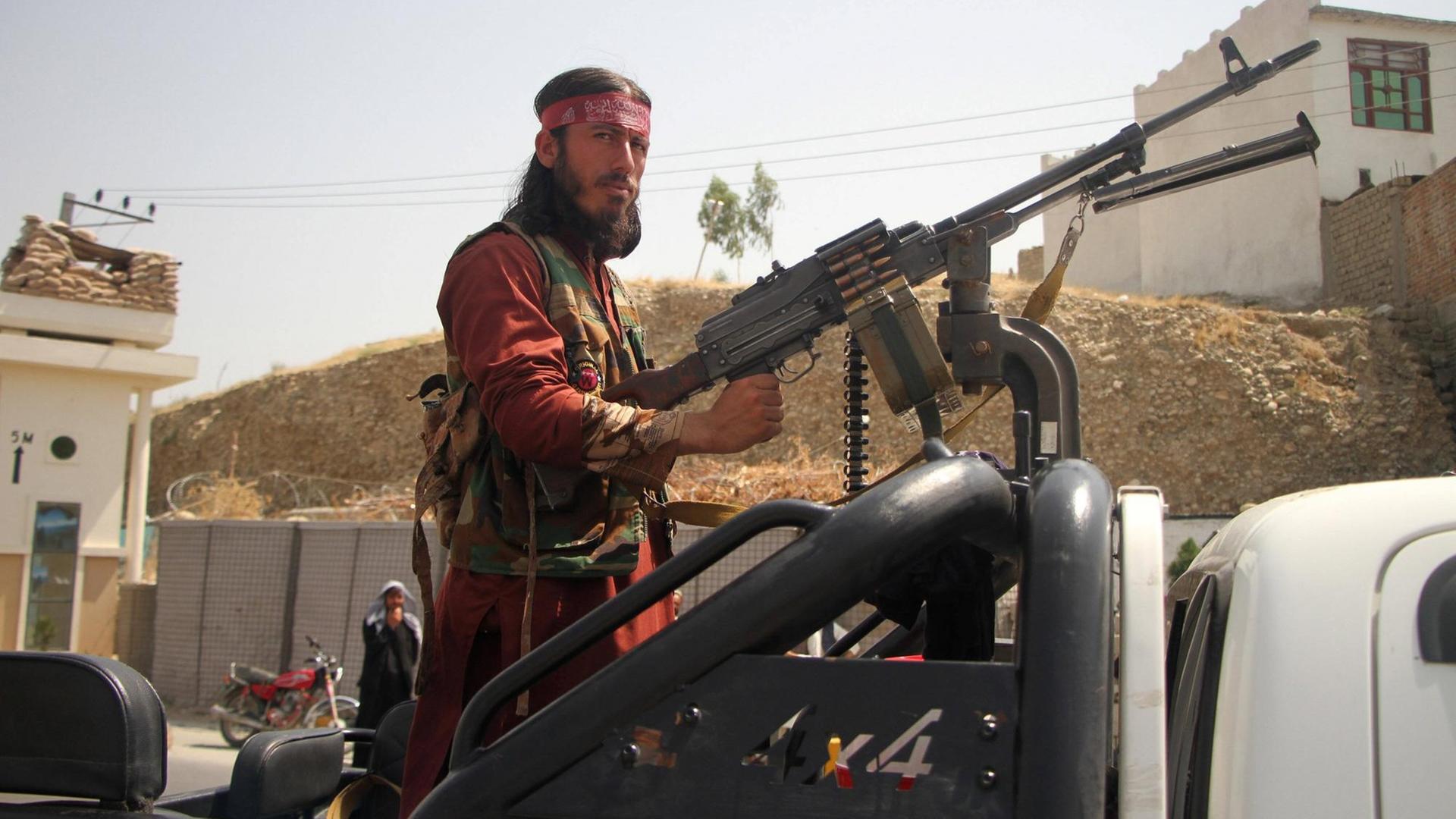 Ein Talban steht an einem großen Maschinengewehr und blickt ernst in die Kamera.