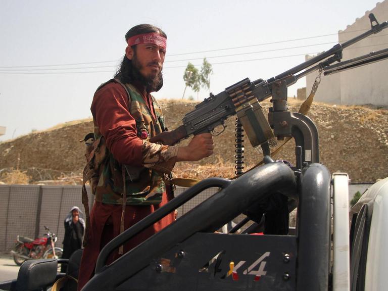 Ein Talban steht an einem großen Maschinengewehr und blickt ernst in die Kamera.