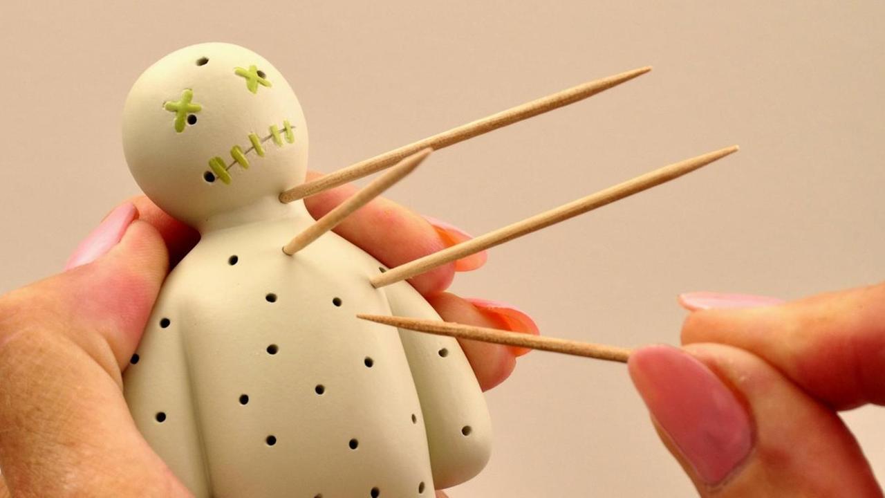 Eine Frauenhand sticht mit Zahnstochern in eine Voddoo-Puppe. Eine Frauenhand sticht mit Zahnstochern in eine Voddoo-Puppe.