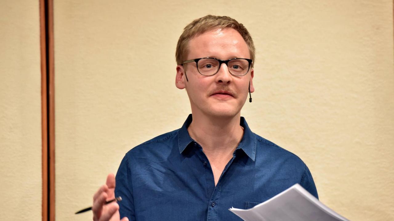 Der Journalist Florian Kessler während einer Lesung auf der Bühne. Der Journalist Florian Kessler während einer Lesung auf der Bühne.