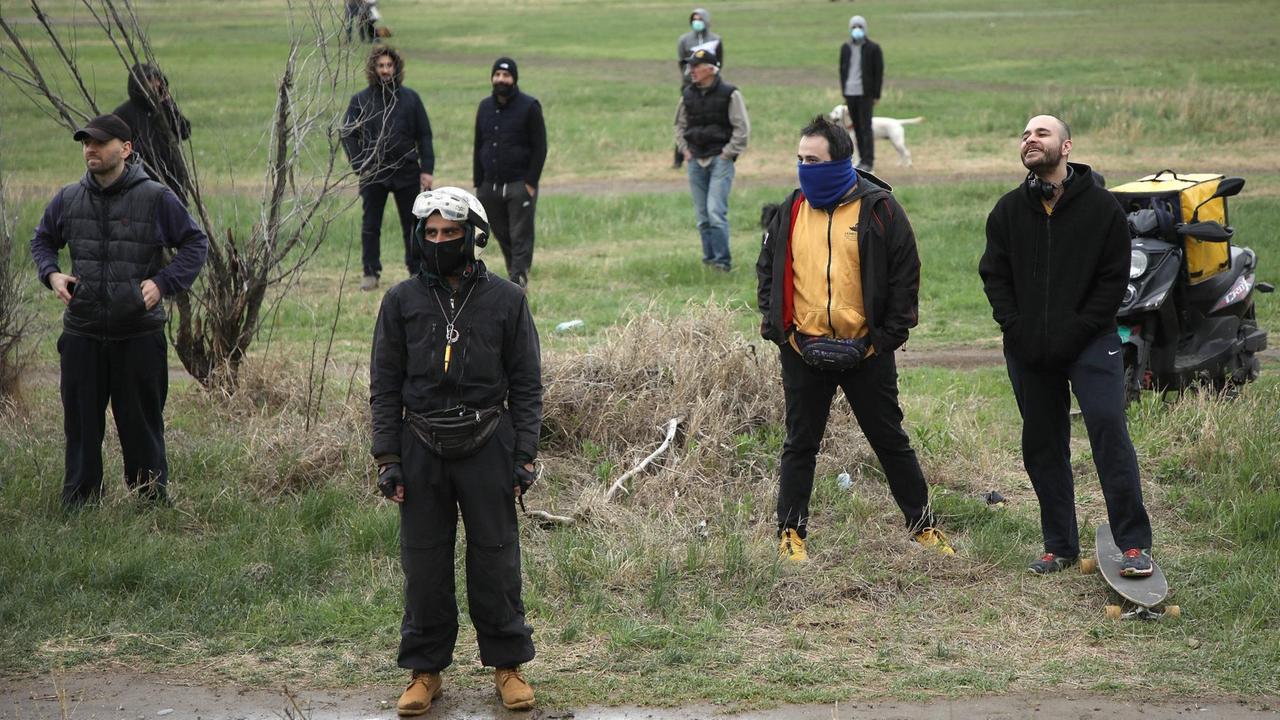 Eine Gruppe junger, schwarz gekleideter Menschen steht verstreut auf einer sumpfigen Wiese. Eine Gruppe junger, schwarz gekleideter Menschen steht verstreut auf einer sumpfigen Wiese.