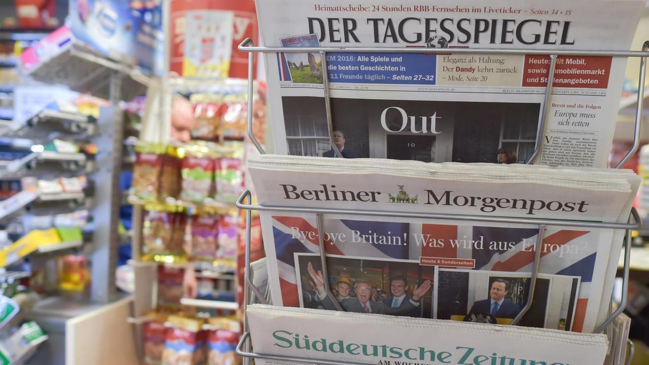In dem Ständer klemmen der Tagesspiegel, die Berliner Morgenpopst und die Süddeutsche Zeitung. Im Hintergrund unscharf Süssigkeitenregale. In dem Ständer klemmen der Tagesspiegel, die Berliner Morgenpopst und die Süddeutsche Zeitung. Im Hintergrund unscharf Süssigkeitenregale.