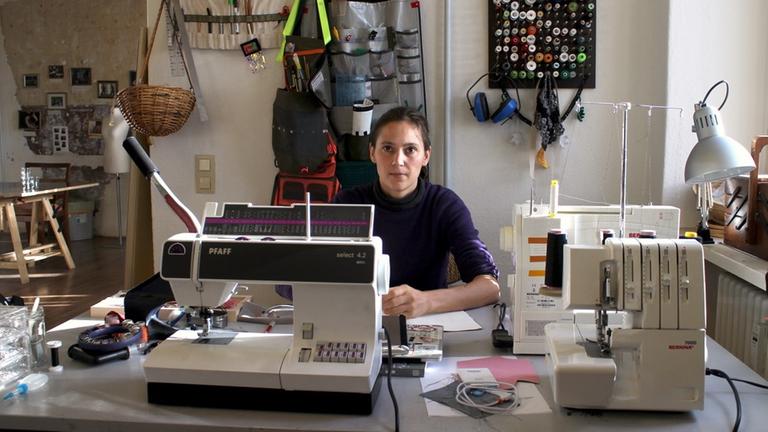 Eine junge Frau sitzt an einer Nähmaschine in ihrem Atelier Eine junge Frau sitzt an einer Nähmaschine in ihrem Atelier