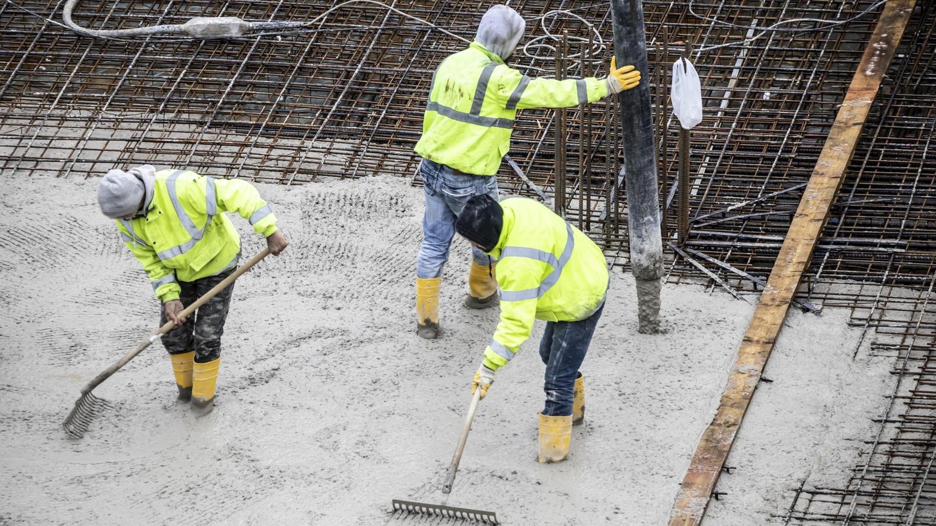 Drei Menschen stehen auf einer Baustelle. Sie gießen gerade das Beton-Fundament eines Gebäudes. Drei Menschen stehen auf einer Baustelle. Sie gießen gerade das Beton-Fundament eines Gebäudes.