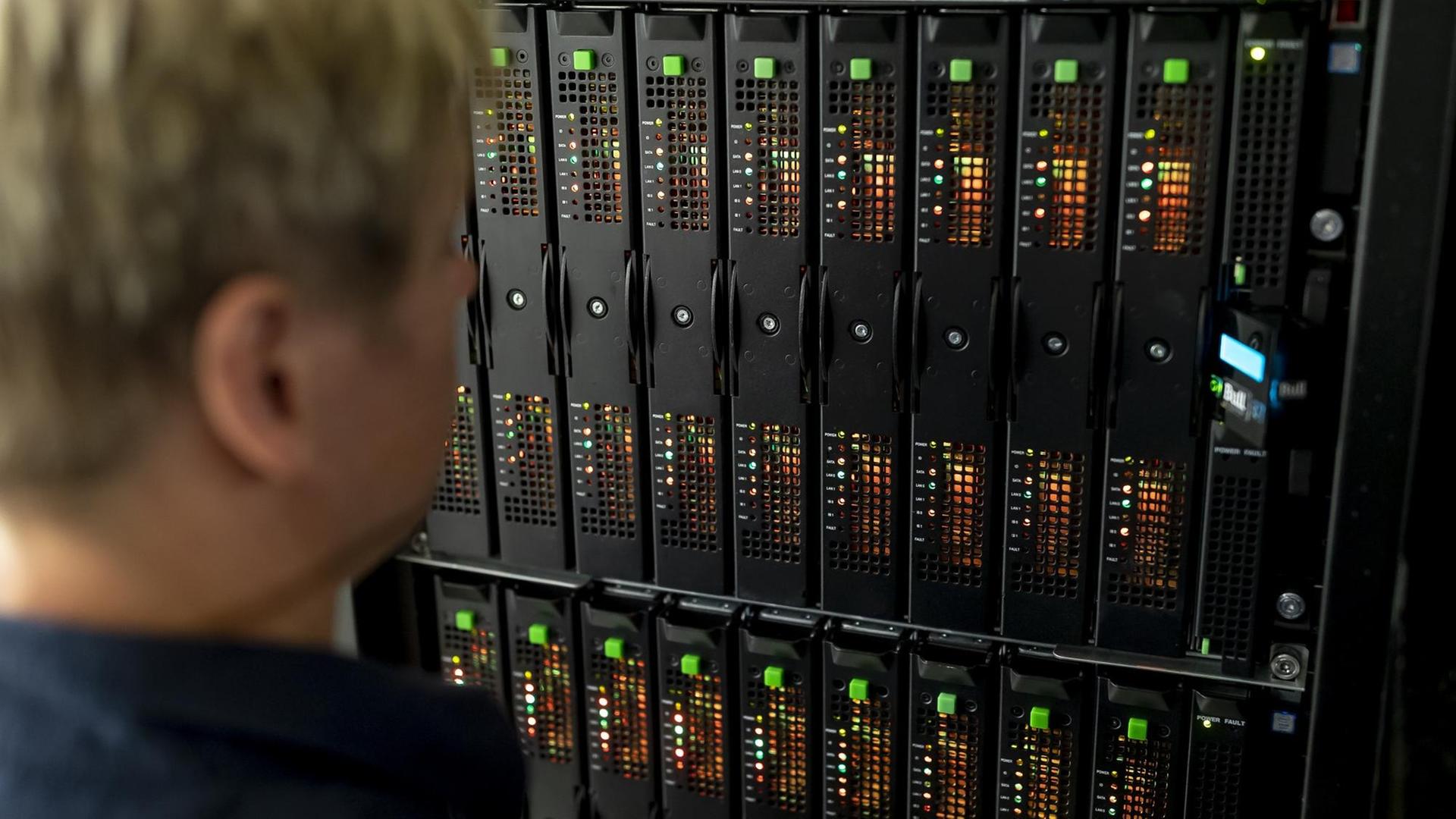 Eine Mitarbeiterin steht vor einem Rechnerschrank und schaut auf Leuchtdioden der Prozessoren des Supercomputers "Mistral" im Deutschen Klimazentrum in Hamburg