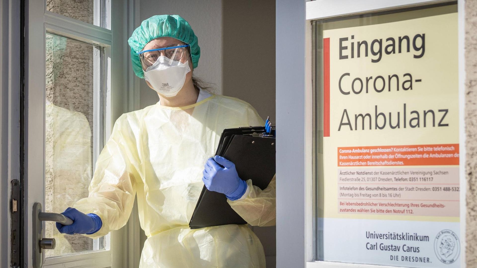 Eine Infektiologin in Schutzausrüstung steht mit vorgefertigten Fragebögen in der Eingangstür der Corona-Ambulanz an der Uniklinik Dresden. Eine Infektiologin in Schutzausrüstung steht mit vorgefertigten Fragebögen in der Eingangstür der Corona-Ambulanz an der Uniklinik Dresden.