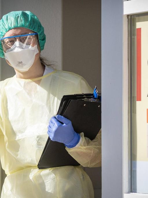 Eine Infektiologin in Schutzausrüstung steht mit vorgefertigten Fragebögen in der Eingangstür der Corona-Ambulanz an der Uniklinik Dresden.