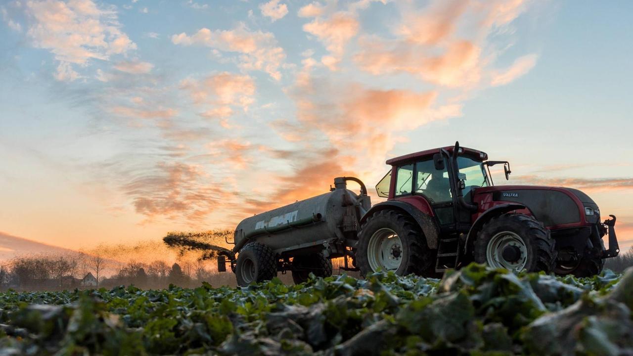 Landwirt fährt mit einem Güllefass bei Sonnenaufgang über ein angefrorenes Feld Landwirt fährt mit einem Güllefass bei Sonnenaufgang über ein angefrorenes Feld