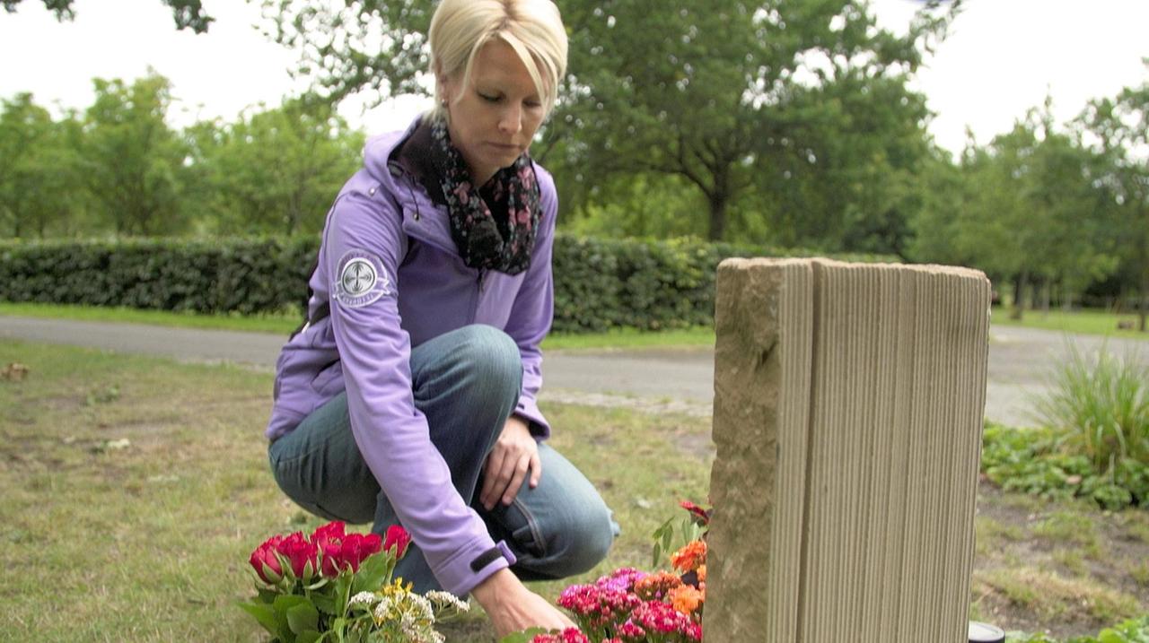 Eine Frau legt Blumen am Grab ihres Vaters ab.