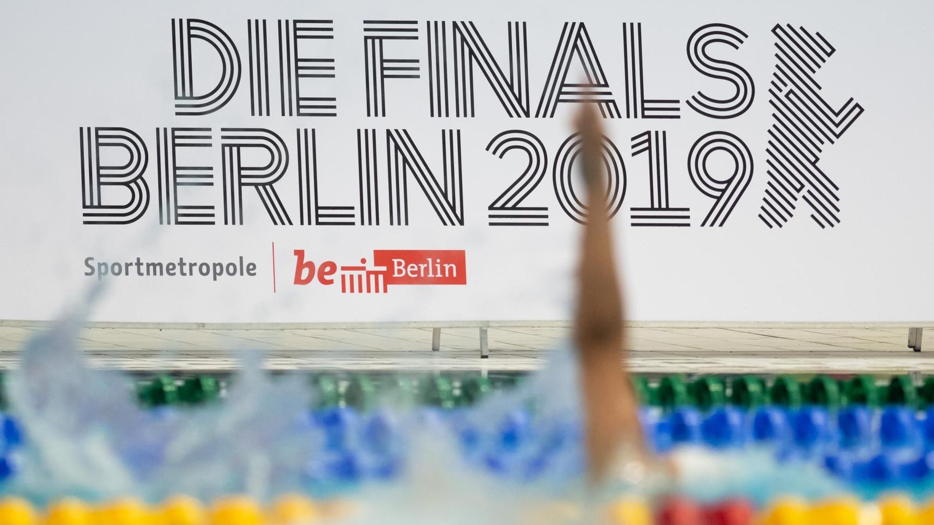 Blick auf das Veranstaltungslogo "Die Finals Berlin 2019", davor ist ein Schwimmbecken zu sehen, in dem gerade ein Wettkampf stattfindet