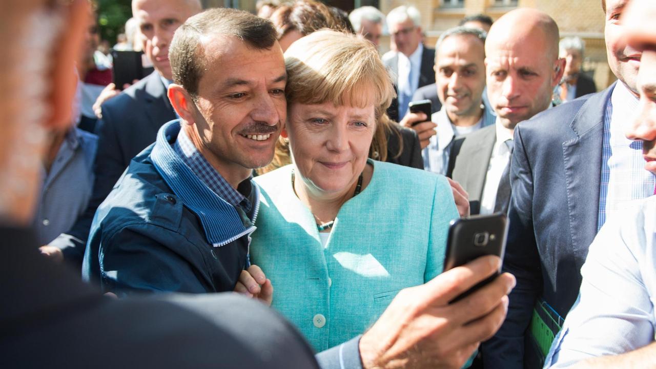 Bundeskanzlerin Merkel und ein Flüchtling blicken Kopf an Kopf in die Handykamera des Mannes.