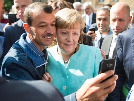 Bundeskanzlerin Merkel und ein Flüchtling blicken Kopf an Kopf in die Handykamera des Mannes.