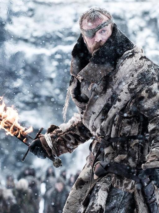 Ein "Game of Thrones"-Charakter mit Augenklappe steht in einer Eislandschaft und hält ein brennendes Schwert in der Hand