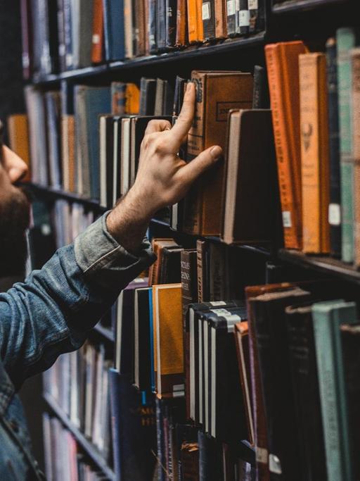 Ein junger Mann zieht ein gebundenes altes Buch aus einem Bibliotheksregal.