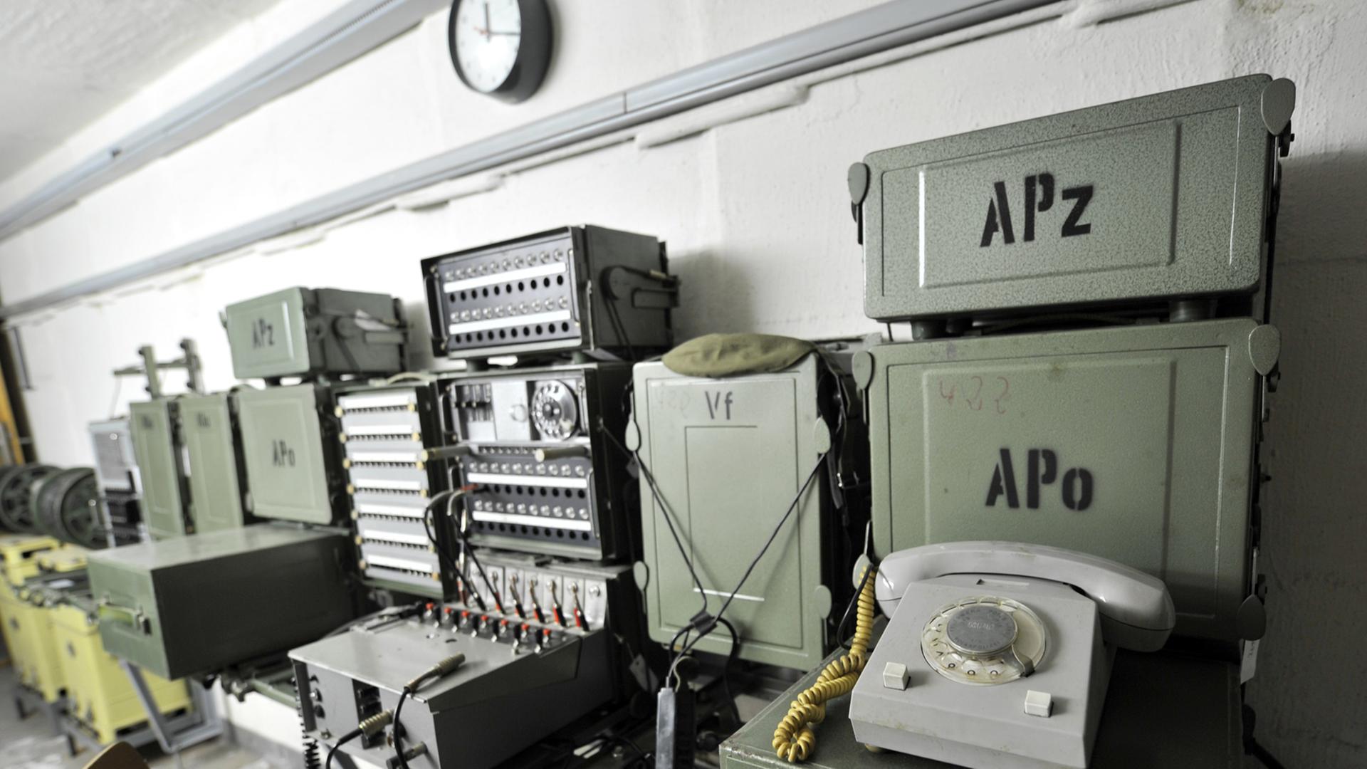 In einem Bunker sind an einer Wand ein Telefon und mehrere andere elektronische Geräte angebracht. In einem Bunker sind an einer Wand ein Telefon und mehrere andere elektronische Geräte angebracht.
