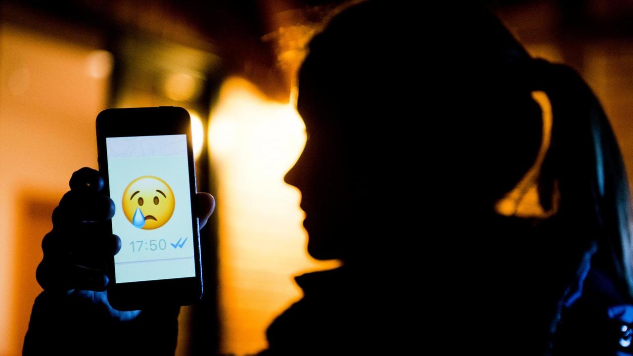 ILLUSTRATION - Ein junges Mädchen zeigt am 04.02.2017 das Display eines Smartphones mit einem weinenden Emoji beim Messenger «WhatsApp» (gestellte Szene). Wenn falsche Behauptungen oder Beleidigungen über einen Menschen in sozialen Netzwerken, bei Messengern wie WhatsApp und anderen Online-Diensten verbreitet werden, sprechen Fachleute von Cybermobbing. Am 7. Februar findet der Safer Internet Day mit dem Schwerpunktthema Cybermobbing statt. ILLUSTRATION - Ein junges Mädchen zeigt am 04.02.2017 das Display eines Smartphones mit einem weinenden Emoji beim Messenger «WhatsApp» (gestellte Szene). Wenn falsche Behauptungen oder Beleidigungen über einen Menschen in sozialen Netzwerken, bei Messengern wie WhatsApp und anderen Online-Diensten verbreitet werden, sprechen Fachleute von Cybermobbing. Am 7. Februar findet der Safer Internet Day mit dem Schwerpunktthema Cybermobbing statt.