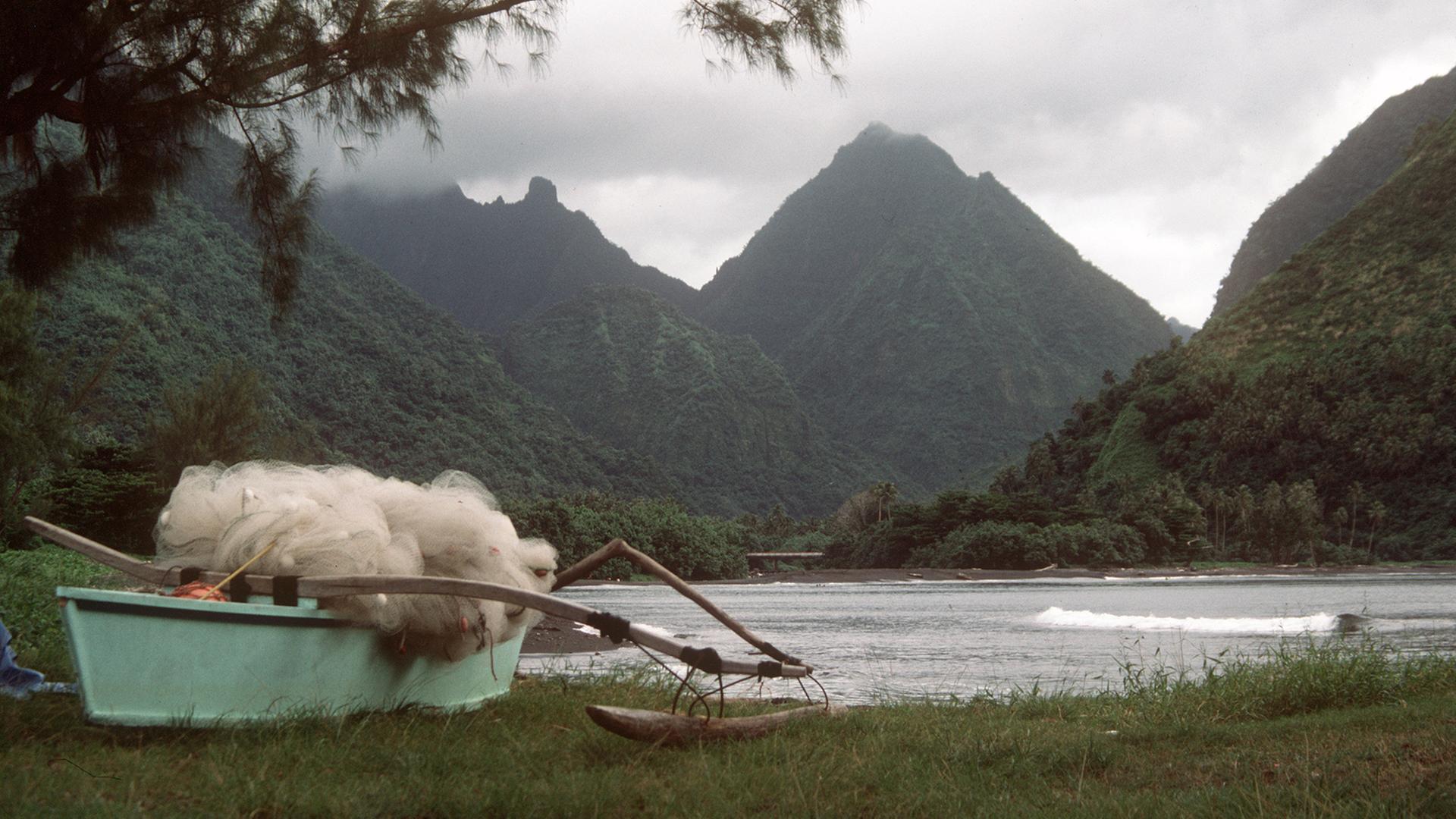 Eine Bucht in Tahiti mit dichter Vegetation und bizarr geformten Bergen, im Vordergrund ein typisches Auslegerboot mit Netzen von Fischern der einheimischen Bevölkerung. Aufnahme von 1985. Eine Bucht in Tahiti mit dichter Vegetation und bizarr geformten Bergen, im Vordergrund ein typisches Auslegerboot mit Netzen von Fischern der einheimischen Bevölkerung. Aufnahme von 1985.