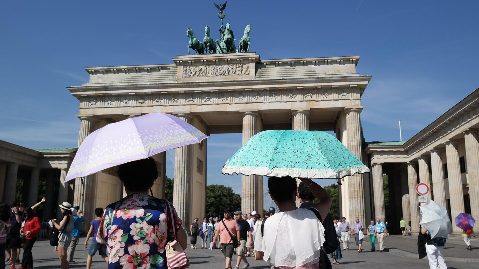 Touristen schützen sich mit Schirmen vor den Sonnenstrahlen vor dem Brandenburger Tor in Berlin. Touristen schützen sich mit Schirmen vor den Sonnenstrahlen vor dem Brandenburger Tor in Berlin.