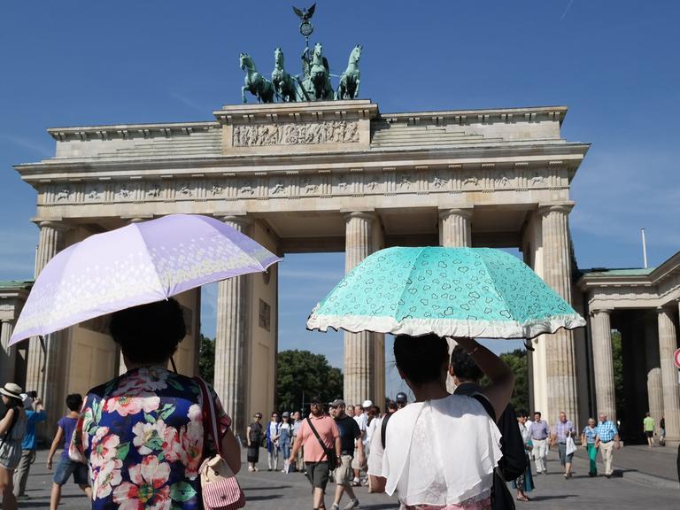Touristen schützen sich mit Schirmen vor den Sonnenstrahlen vor dem Brandenburger Tor in Berlin.