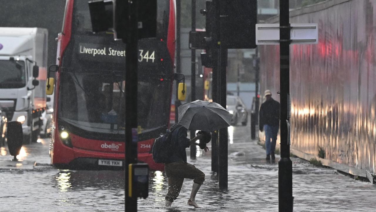 Ein Fußgänger läuft über eine überflutete Straße in London. Im Hintergrund ist ein roter Bus zu sehen. Ein Fußgänger läuft über eine überflutete Straße in London. Im Hintergrund ist ein roter Bus zu sehen.
