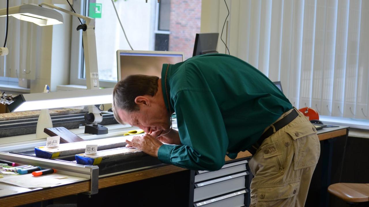 Geologe David Kring nimmt einen aufgeschnittenen Bohrkern unter die Lupe: Analyse von Mikrofossilien (Foraminiferen) aus dem Bohrkern und aus Zeit nach der Katastrophe, als wieder Leben im Krater gefunden wurde Geologe David Kring nimmt einen aufgeschnittenen Bohrkern unter die Lupe: Analyse von Mikrofossilien (Foraminiferen) aus dem Bohrkern und aus Zeit nach der Katastrophe, als wieder Leben im Krater gefunden wurde