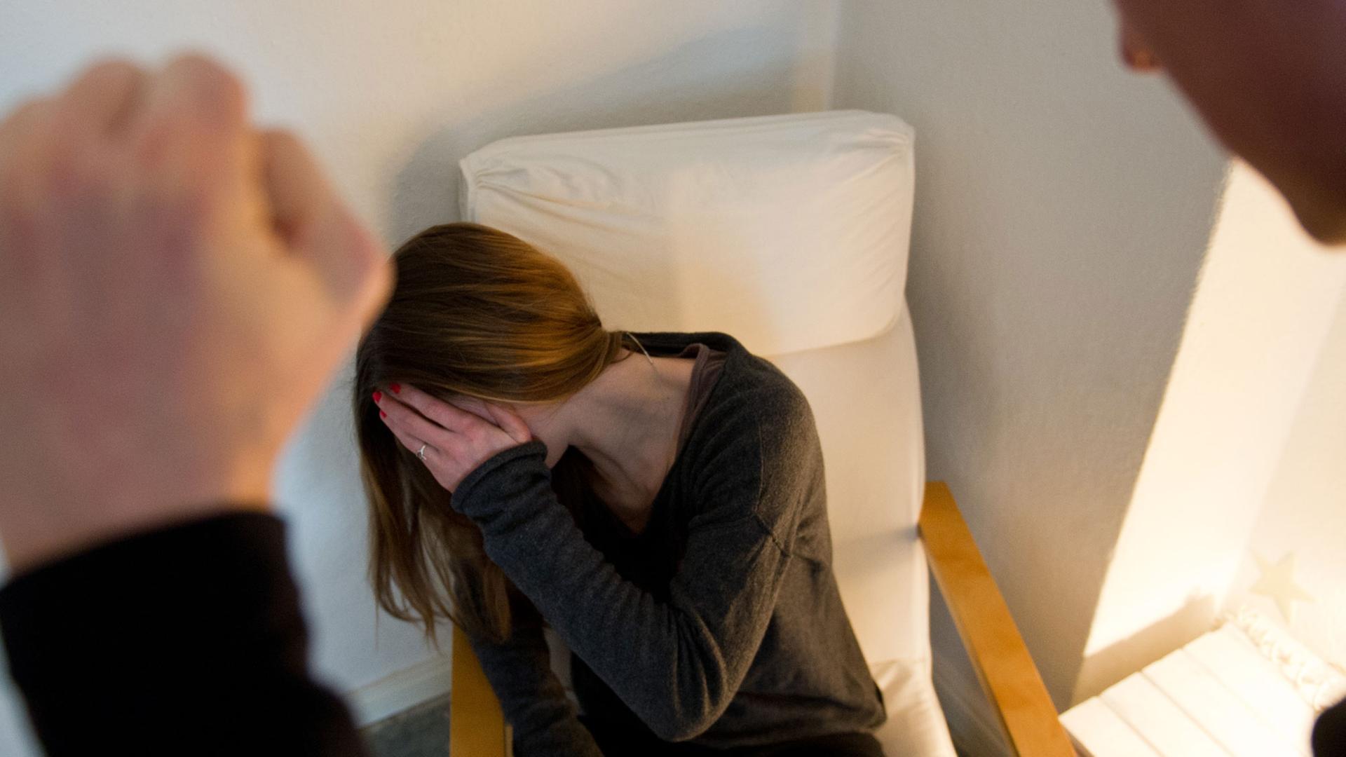 Ein Mann ballt seine Hand zur Faust, vor ihm eine Frau auf einem Sessel, die sich ängstlich die Hand vor ihr Gesicht hält. Ein Mann ballt seine Hand zur Faust, vor ihm eine Frau auf einem Sessel, die sich ängstlich die Hand vor ihr Gesicht hält.