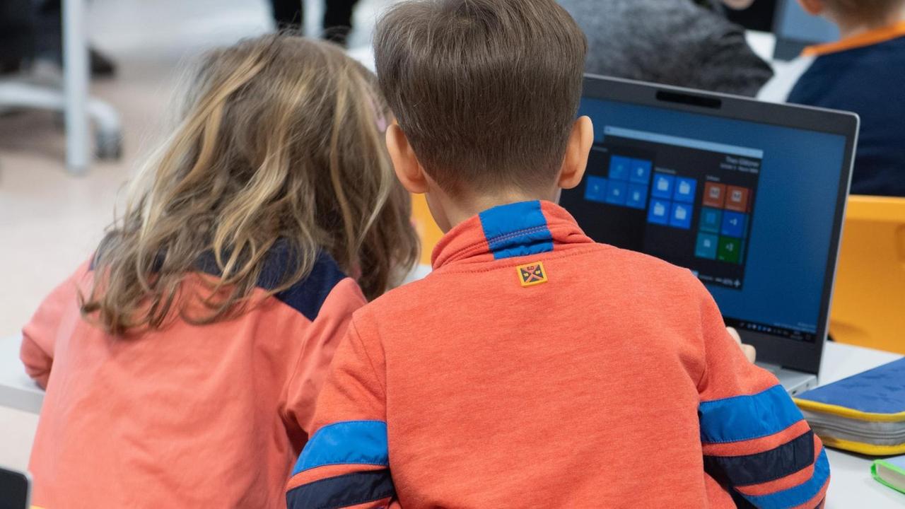 Eine Schülerin und ein Schüler einer dritten Klasse schauen auf einen Laptop. Eine Schülerin und ein Schüler einer dritten Klasse schauen auf einen Laptop.