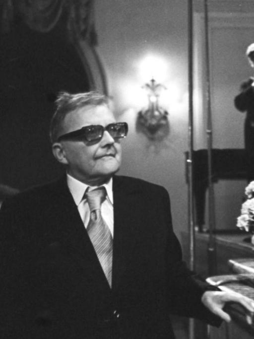 Dmitri Schostakowitsch im Moskauer Konservatorium bei der Uraufführung seiner letzten Sinfonie durch seinen Sohn. Rechts stehen Geiger bereit, links applaudiert das Publikum dem Komponisten.