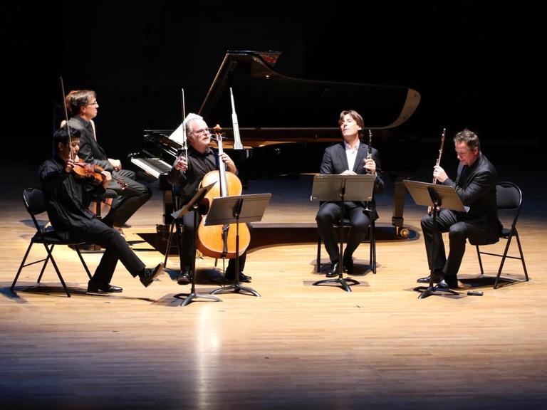 Fünf Musiker sitzen mit ihren Instrumenten auf einer ins Scheinwerferlicht getauchten Bühne.