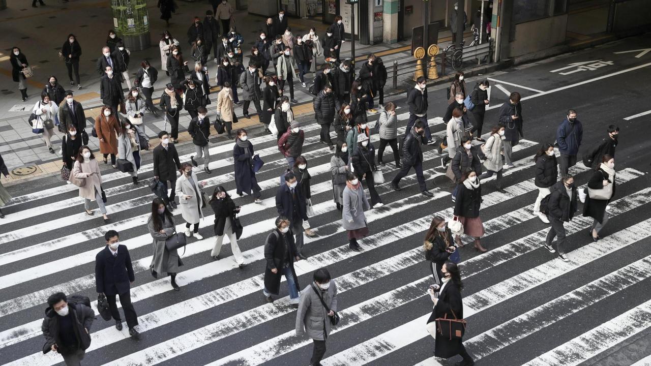 Menschen mit Mund-Nasen-Schutz laufen in Osaka über die Straße.