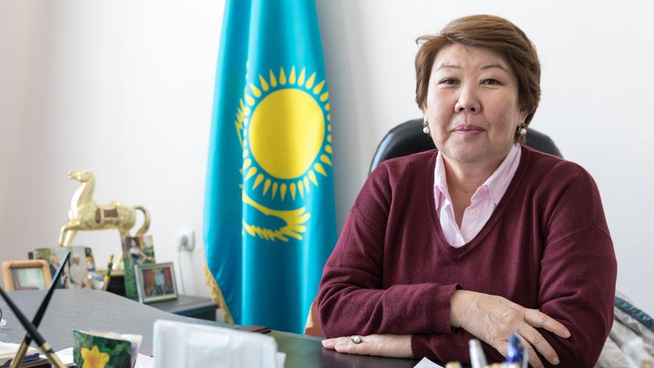 Zauresh Alimbetova ist die Chefin des Naturreservats Barsakelmes - einst eine Insel im Aralsee, soll aus der Wüste künftig eine Sumpflandschaft werden. Sie sitzt im Büro vor einer kasachischen Flagge.