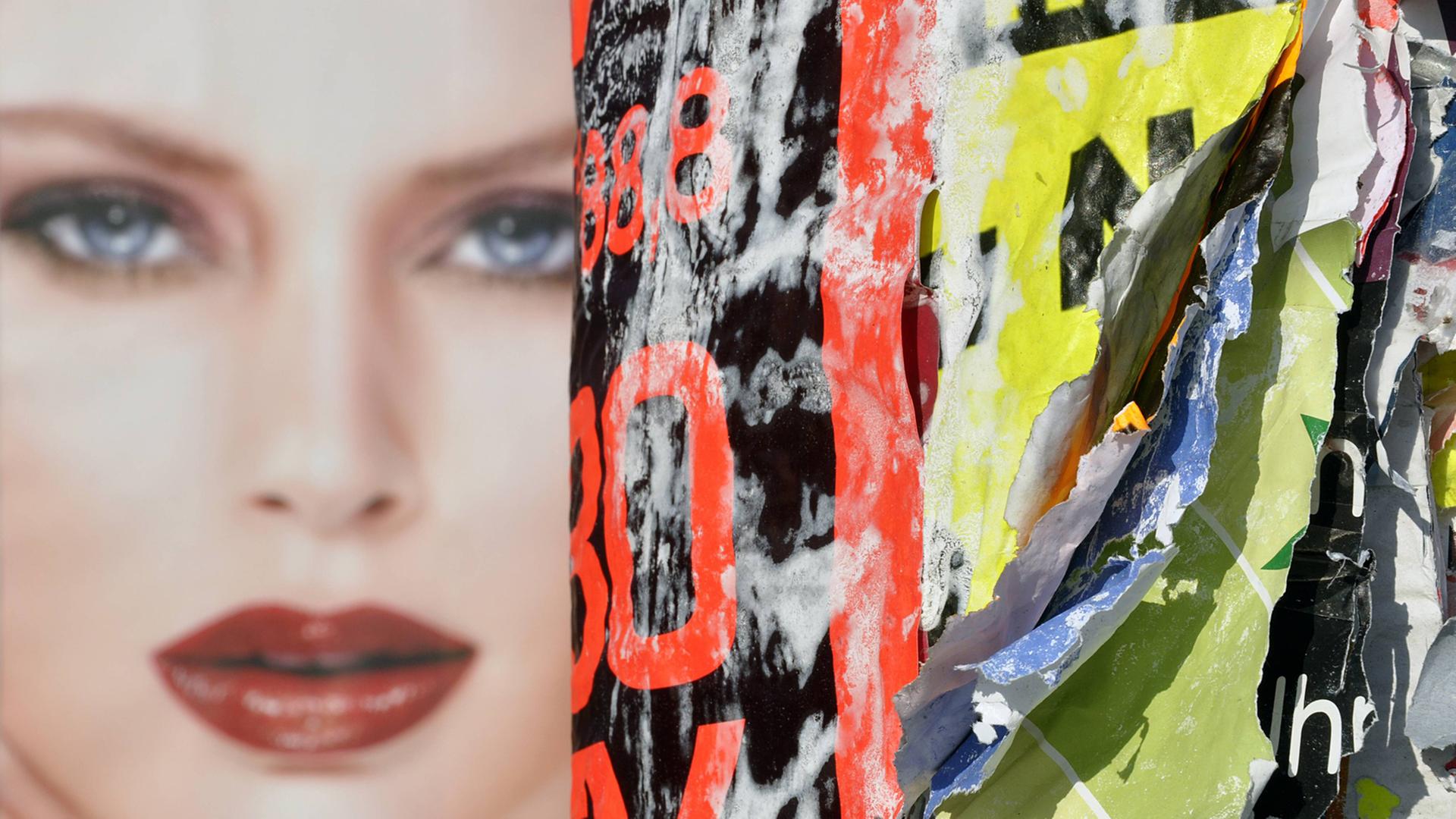Eine Litfasssäule mit abgerissenen Plakaten und dem Foto von einem Gesicht eines Models