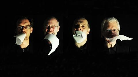 Die Mitglieder des Bremer Ensembles KLANK mit schwarzer Kleidung und einem Papier im Mund