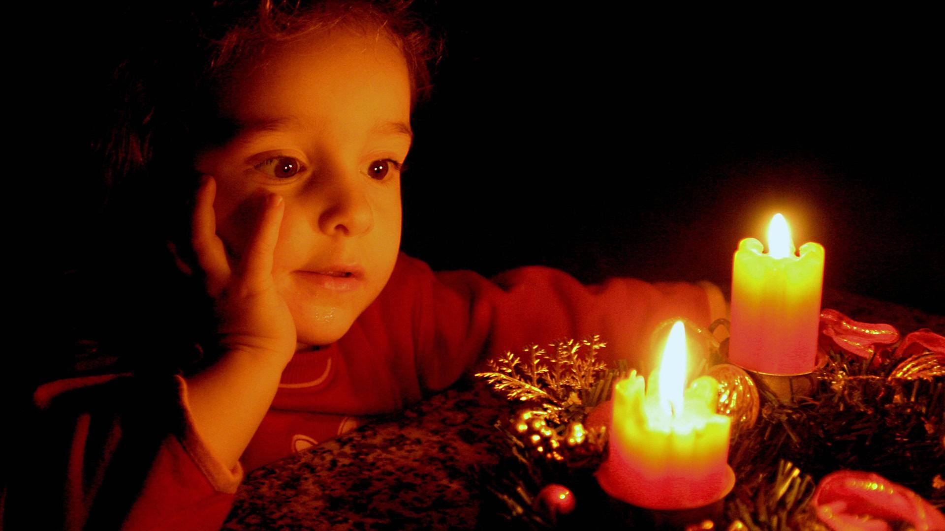 Ein Kind betrachtet brennende Kerzen auf einem Adventskranz.