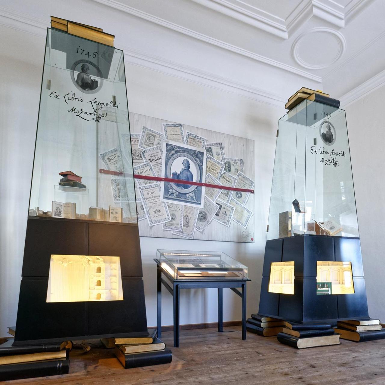 Das Bild zeigt Glasvitrinen mit Büchern und ein Bild, auf dem Leopold Mozart und einige Urkunden abgebildet sind Das Bild zeigt Glasvitrinen mit Büchern und ein Bild, auf dem Leopold Mozart und einige Urkunden abgebildet sind