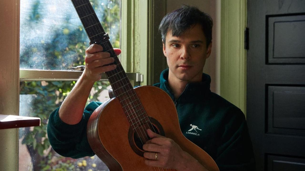 Ein Mann steht vor einem Fenster und spielt eine klassische Gitarre. Ein Mann steht vor einem Fenster und spielt eine klassische Gitarre.